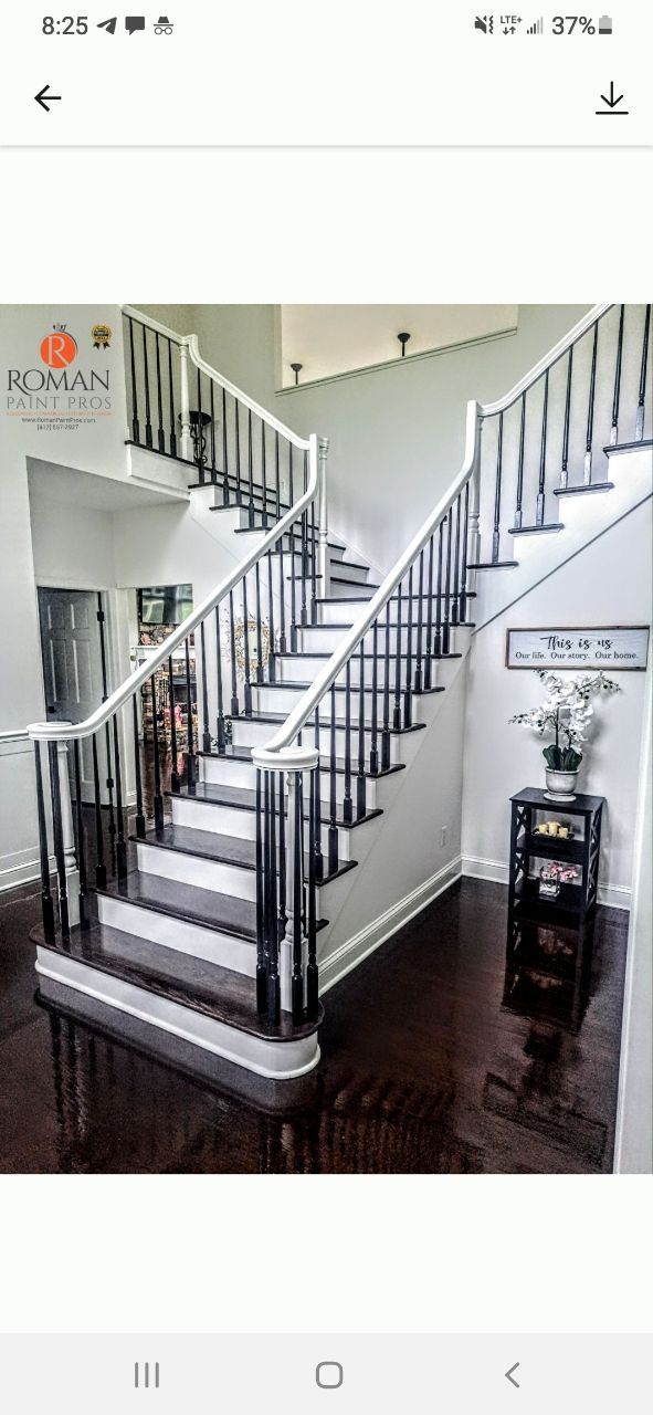 Staircase with white railing and black spindles, dark wood floors, a black cabinet with decor, and a logo on the wall.
