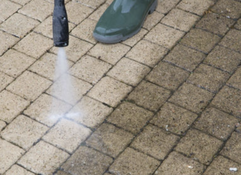 A person pressure washing a brick patio, cleaning the surface.