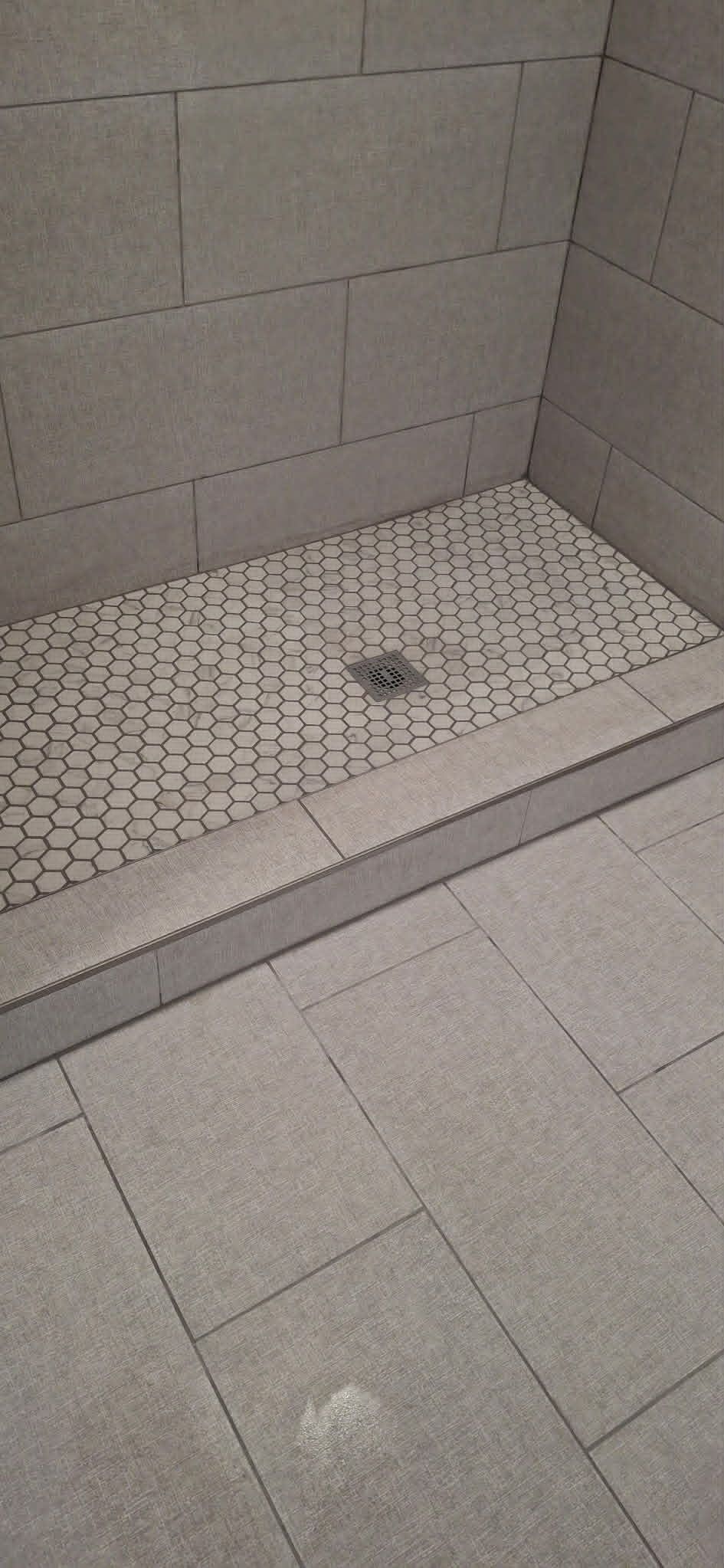 Tiled shower stall with a gray bench and floor drain in the corner.