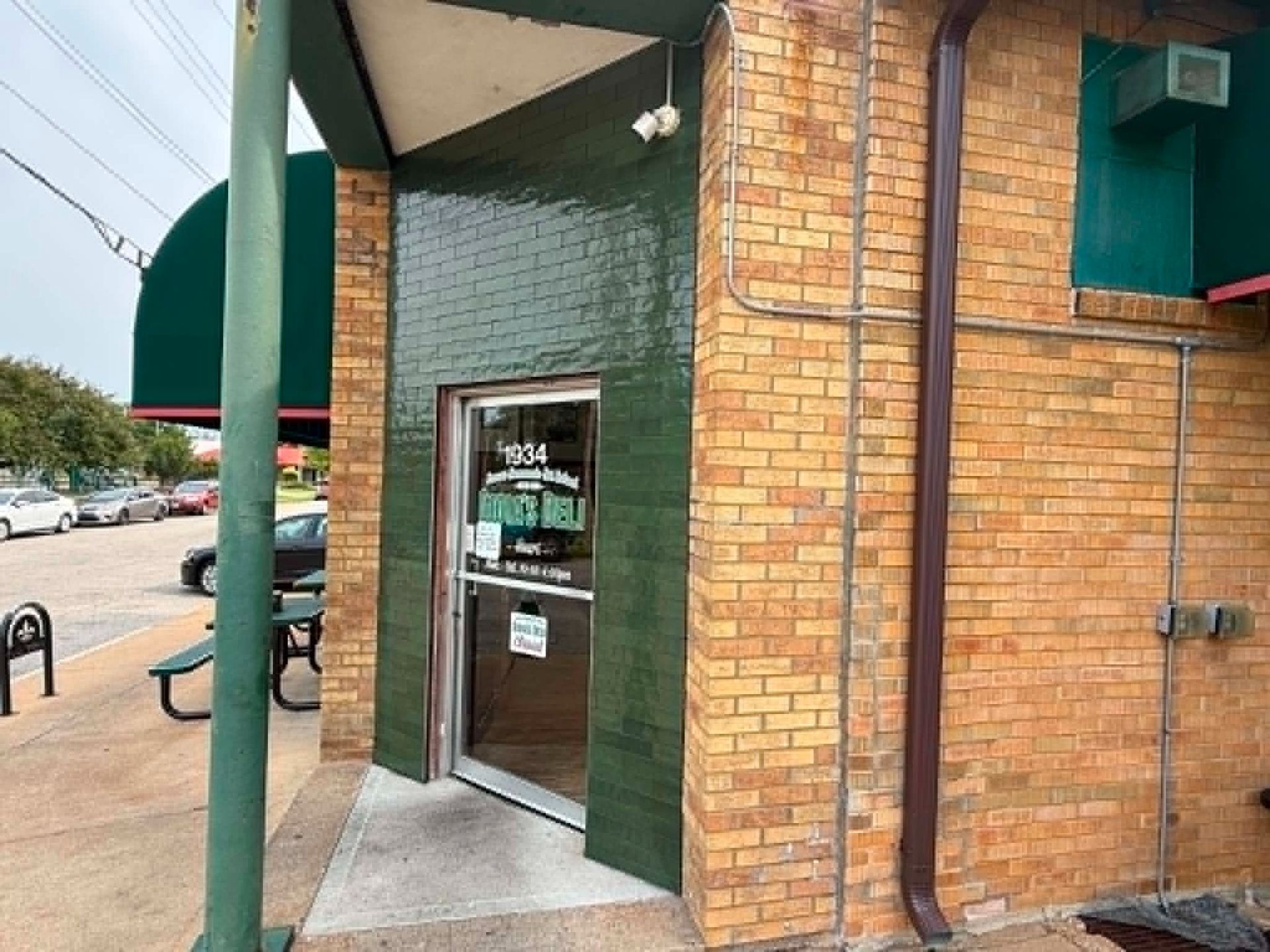 Storefront entrance with glass door, green tile wall, and brick exterior on a sidewalk