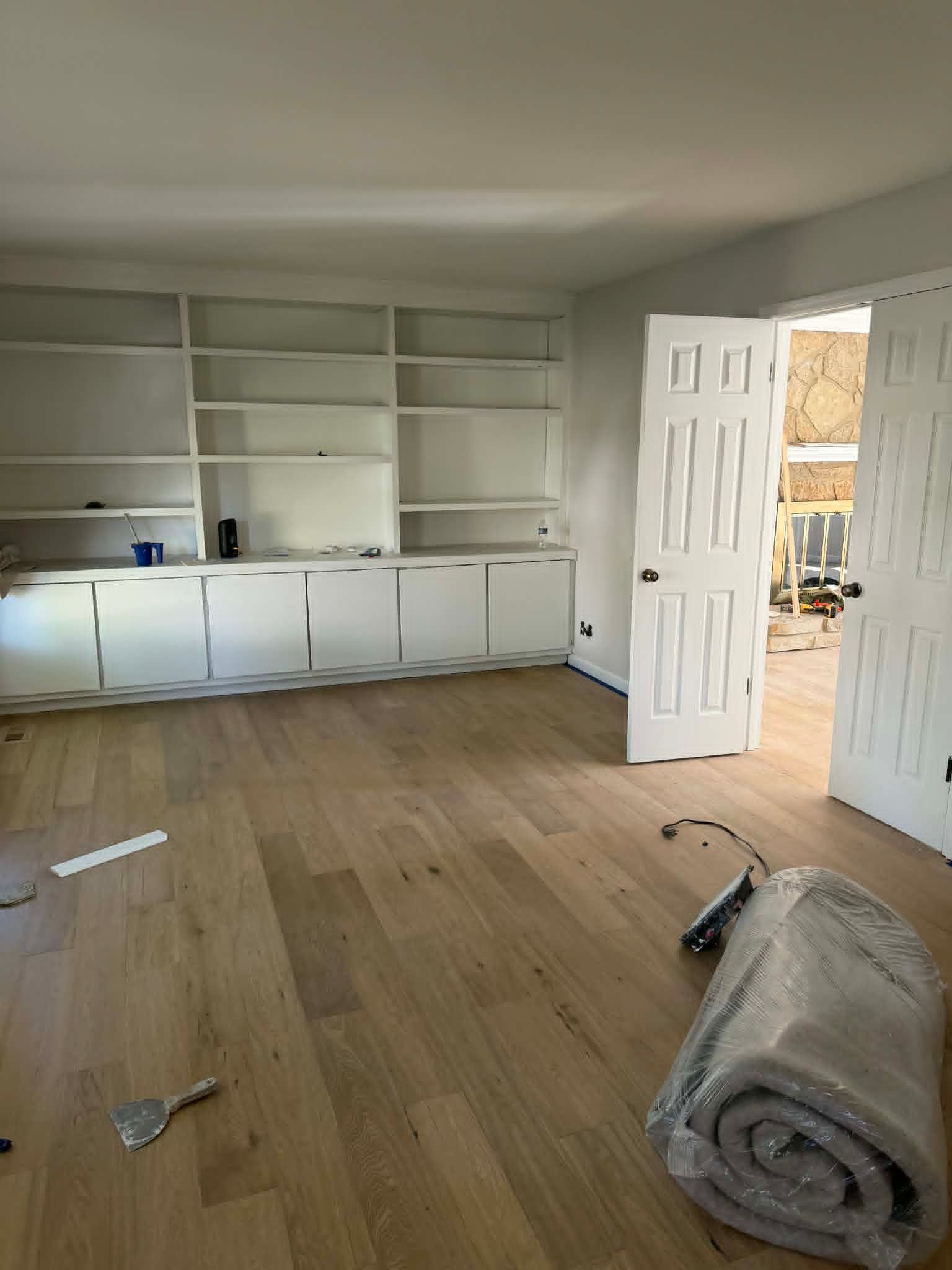 Empty room with white built-in cabinets, open door, and rolled carpet on a wood floor.