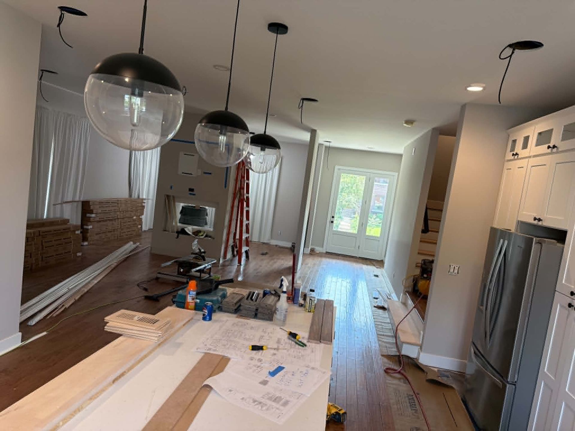 Partially renovated kitchen with white cabinets, hardwood floor, pendant lights, and a long island under construction