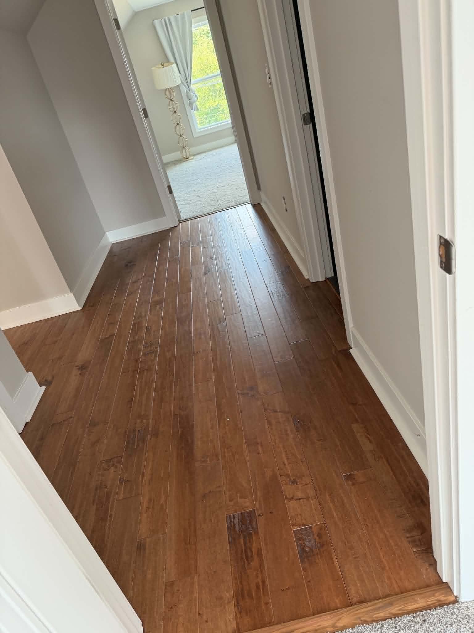 Narrow hallway with wood floors leading to a bright room and glass doors at the end.