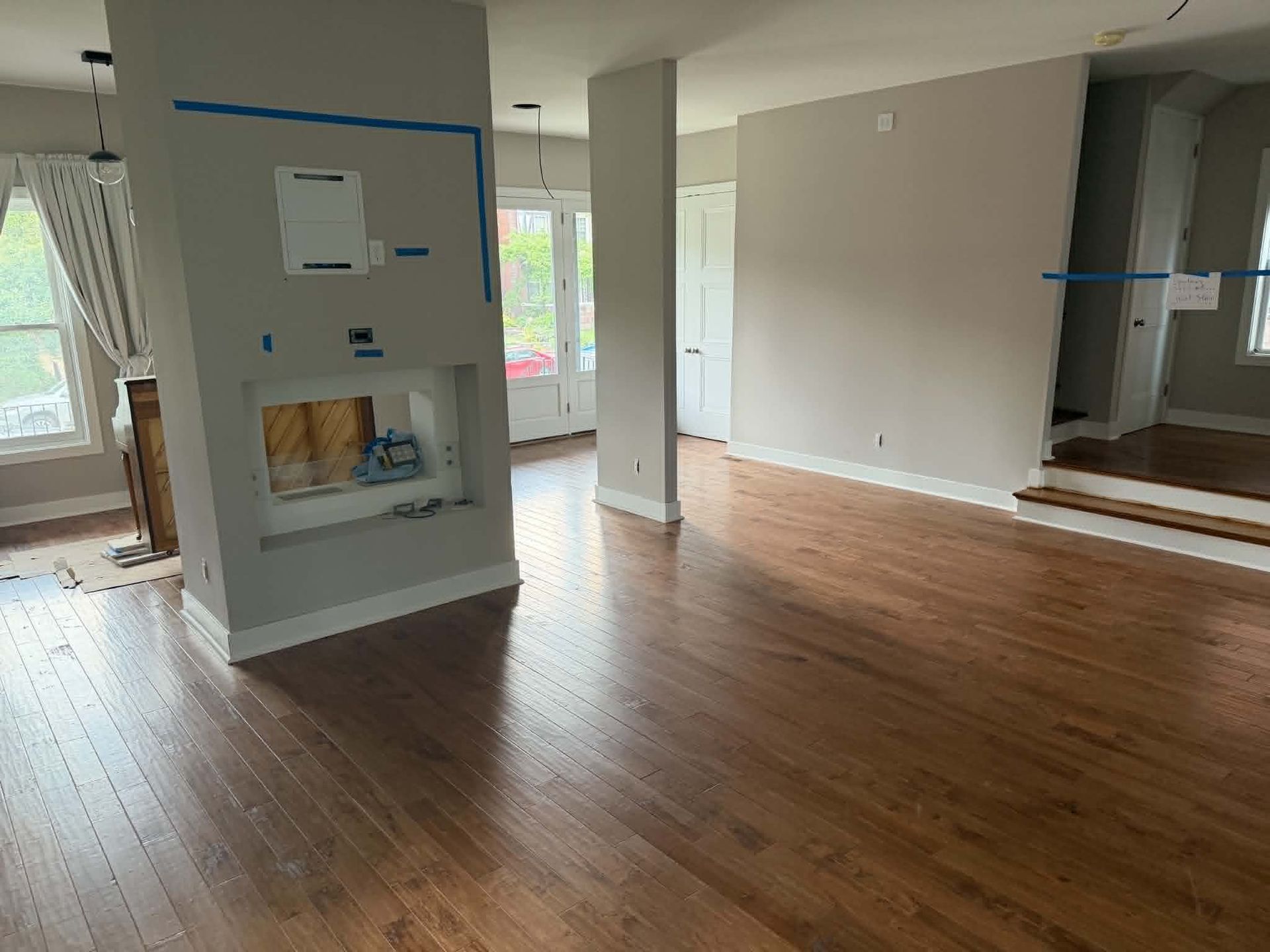 Empty modern living room with hardwood floors, fireplace, and large windows under renovation.