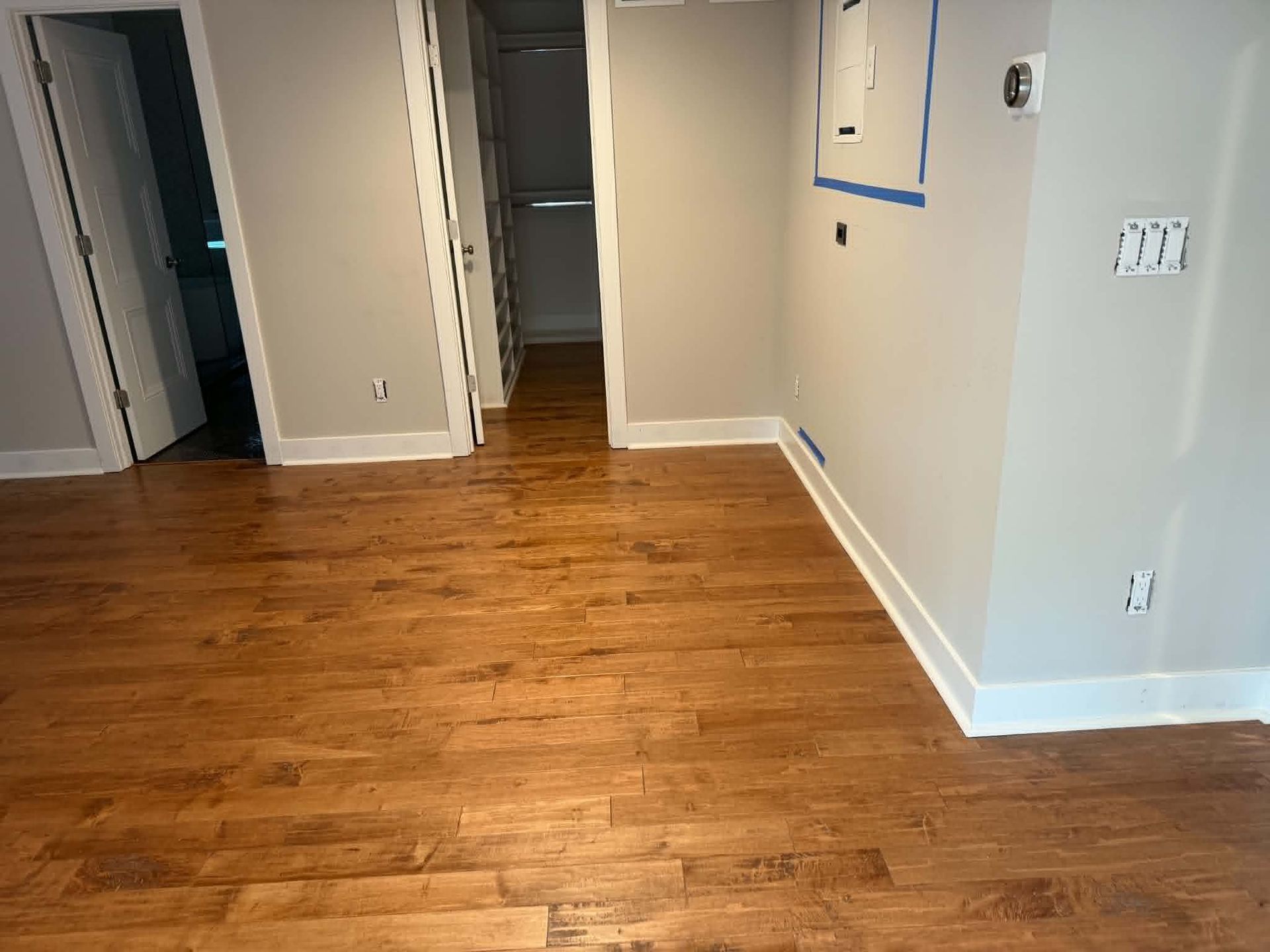 Empty room with wood flooring, beige walls, and open doorways.