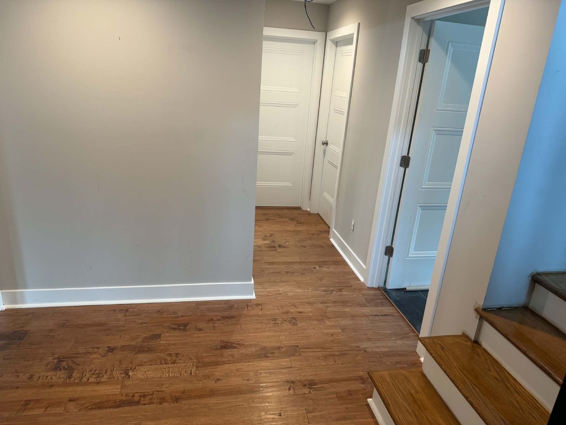 Empty hallway with wood flooring, white walls, and stairs on the right.