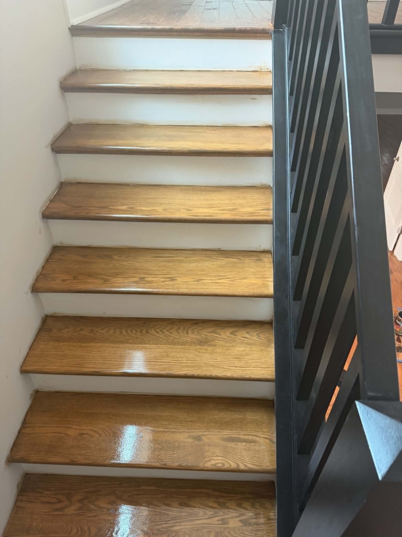 Wooden staircase with white risers and a black railing beside a bright window.