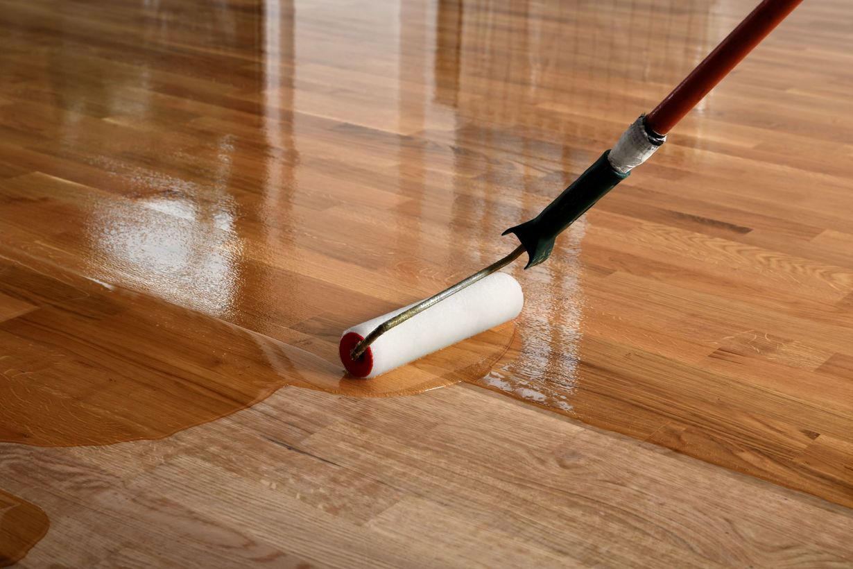 Paint roller applying white finish to a glossy wooden floor