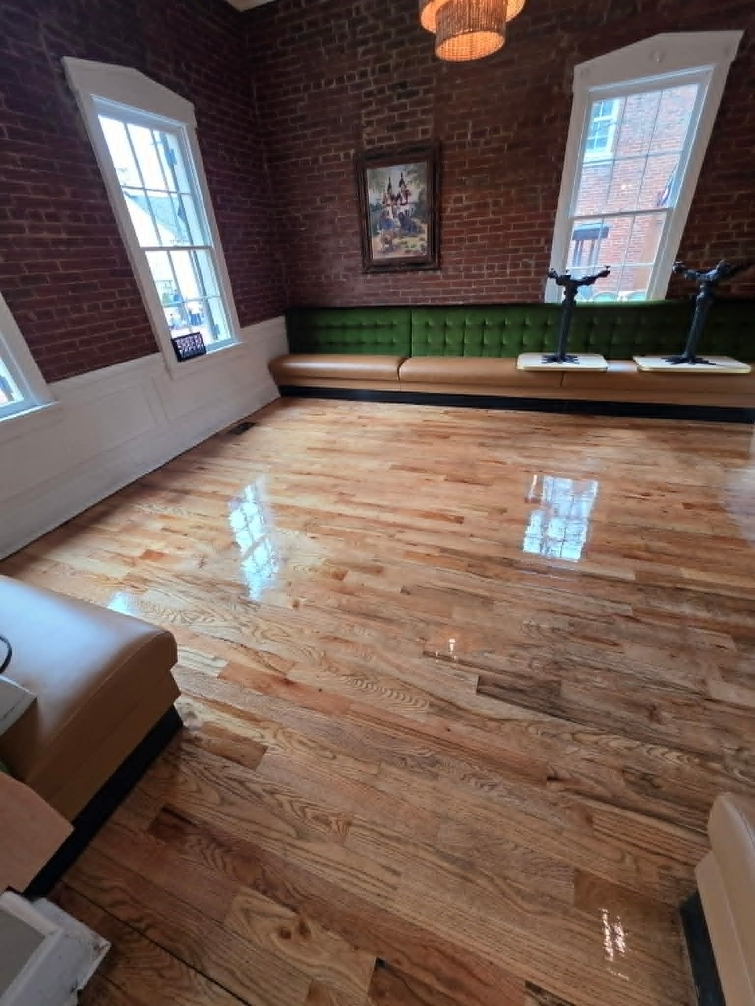 Brick-walled living room with glossy hardwood floors, windows, and a long green sofa seat