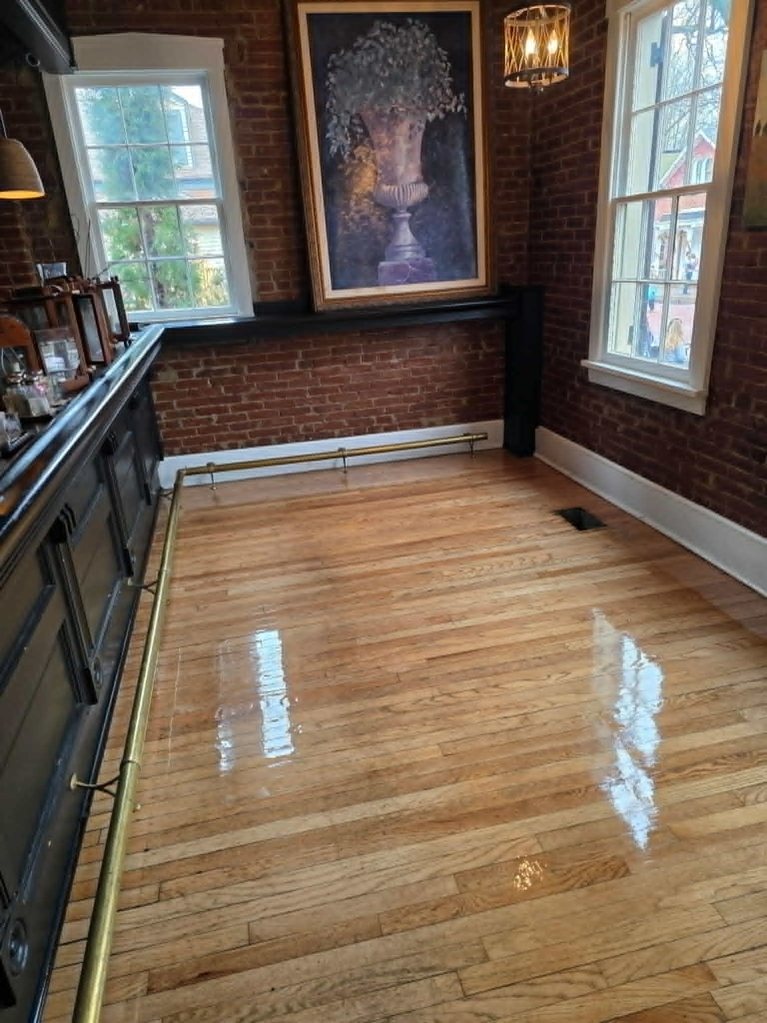 Empty polished wooden hallway with brick walls, large windows, and a framed artwork at the far end