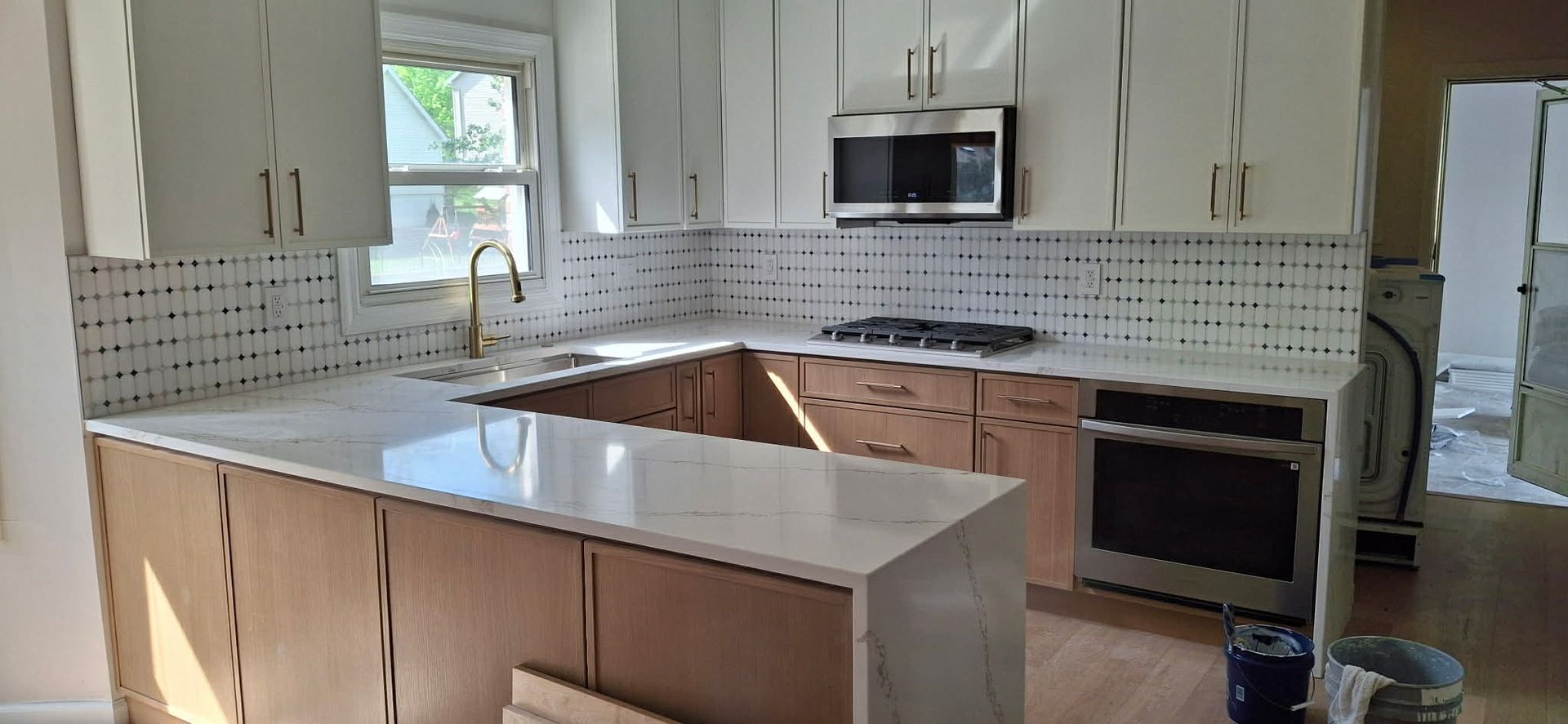 Bright kitchen with white cabinets, island, mosaic backsplash, and stainless steel appliances.