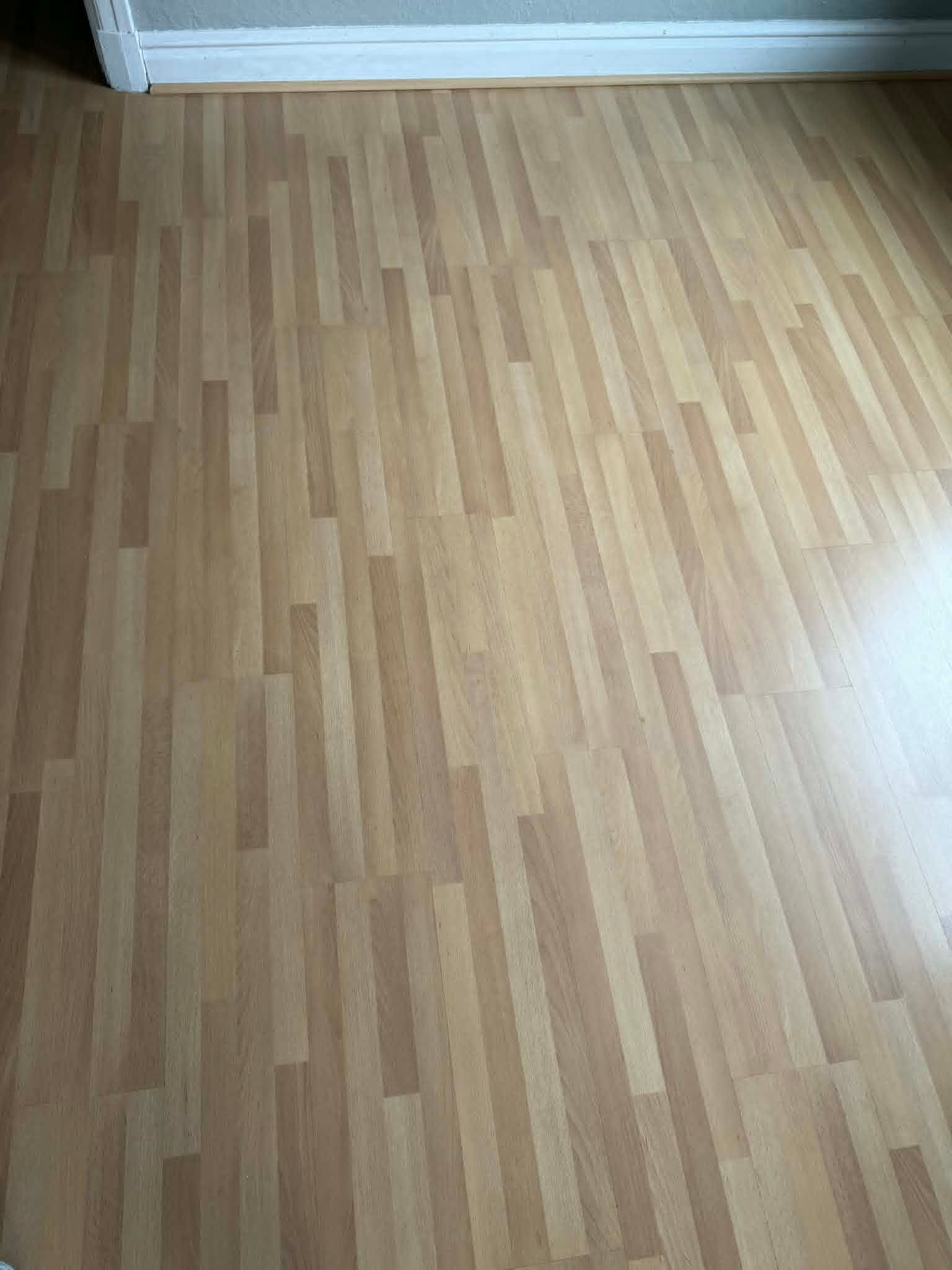 Empty room with light wood flooring and white baseboard trim near a wall.