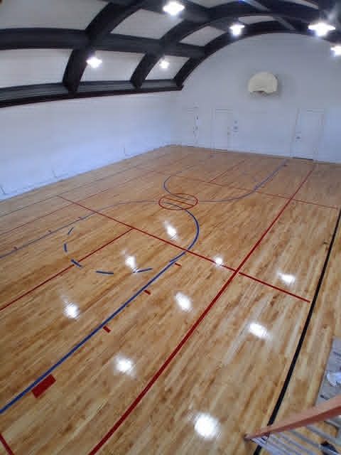 Empty indoor basketball court with polished wood floor and arched ceiling lights