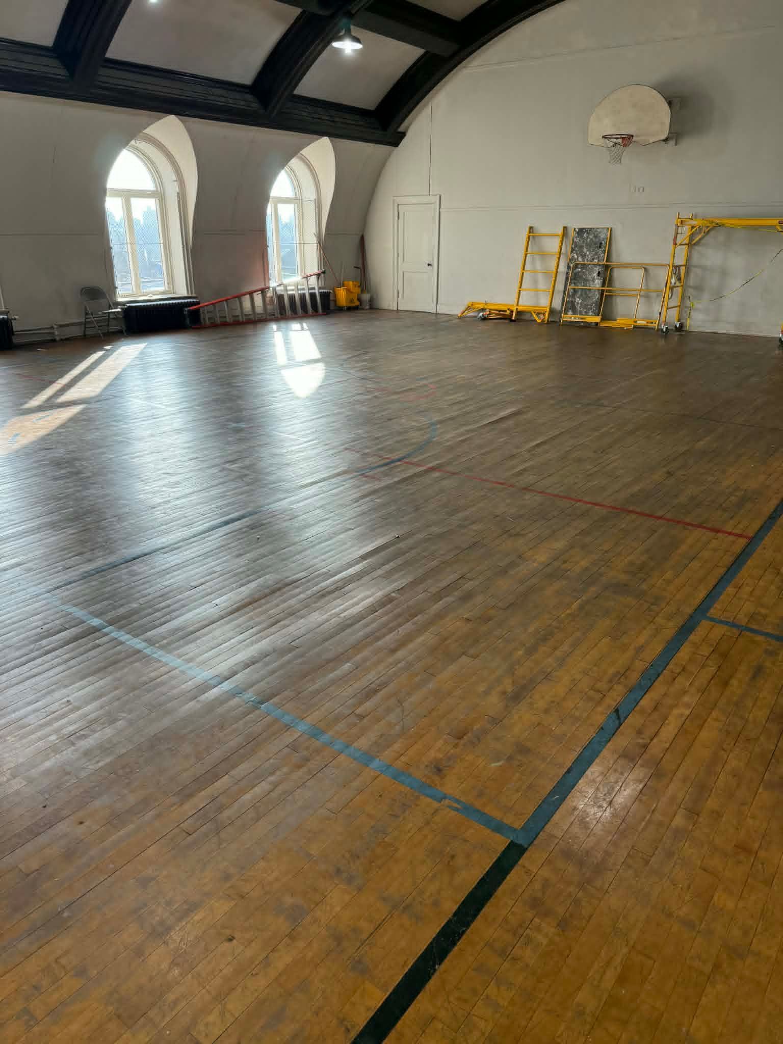 Empty indoor gymnasium with a wooden floor, arched windows, and basketball hoops