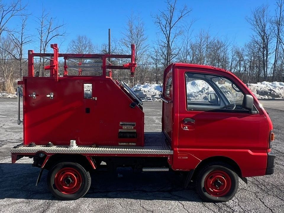 A red truck is parked in a parking lot with trees in the background.