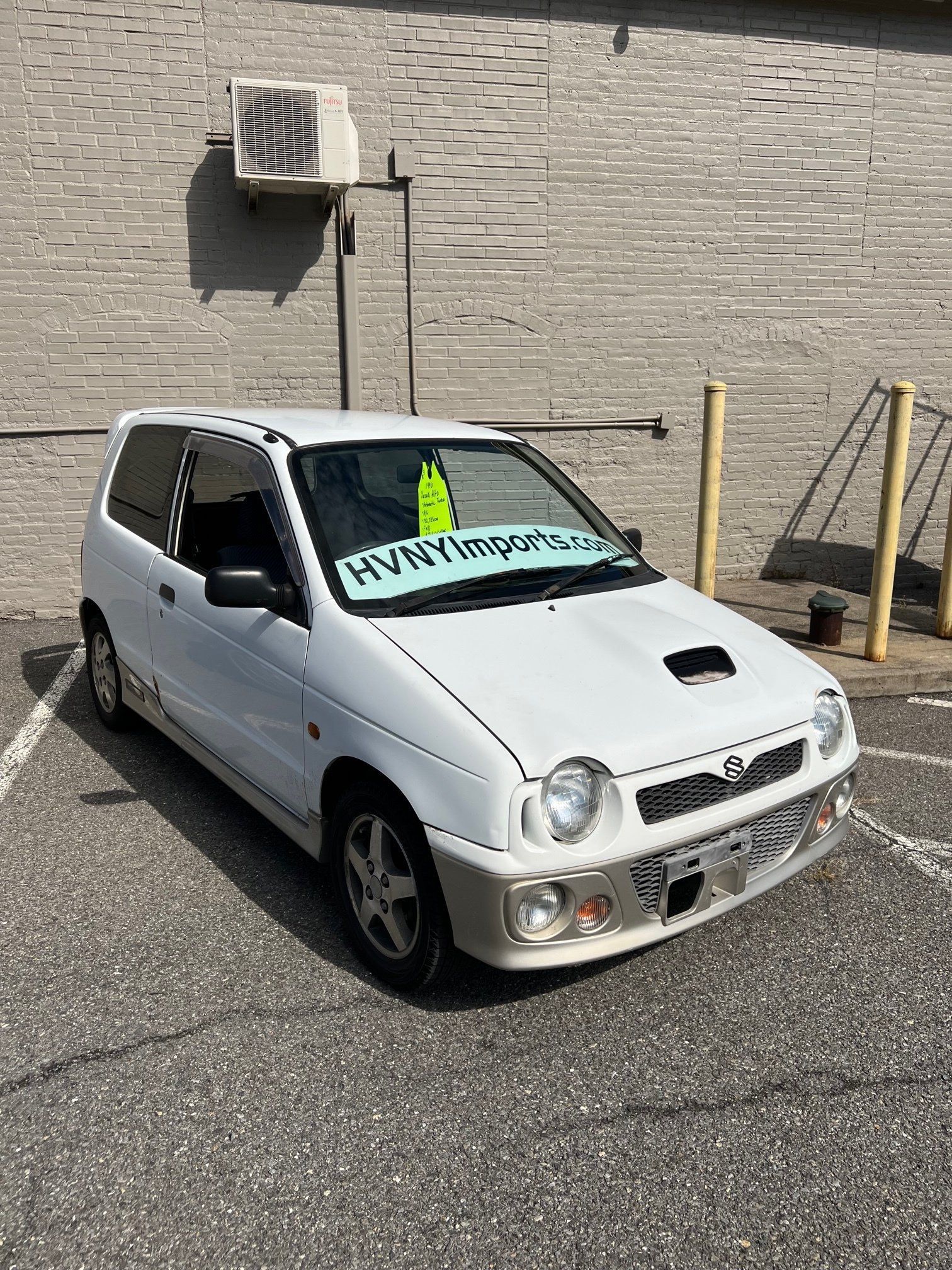 A white car is parked in a parking lot in front of a brick building.