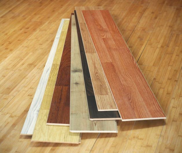 A fan of various wood laminate flooring planks in shades of white, yellow, brown, gray, black, and reddish-brown.