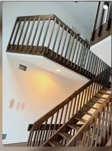 A wooden staircase with matching railings leads up to a landing in a bright, modern interior.