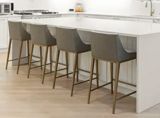 Four gray bar stools with gold-toned legs arranged along a white kitchen island on a light wood floor.