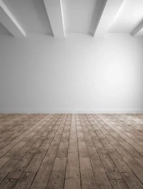 An empty room featuring a worn wooden floor, plain white walls, and exposed ceiling beams.