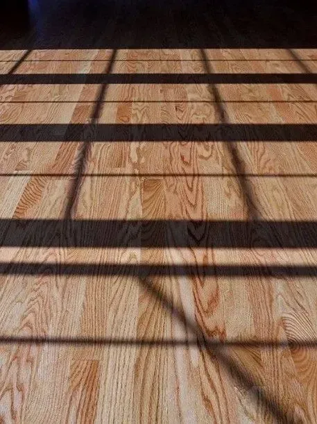 Wooden floorboards with long, dark, parallel shadows cast across them by window blinds.