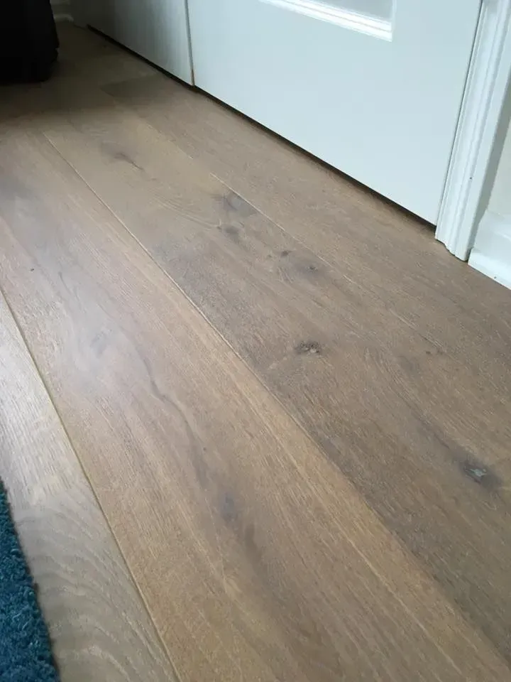 Light brown engineered wood planks with visible grain, installed against white interior trim and doors.