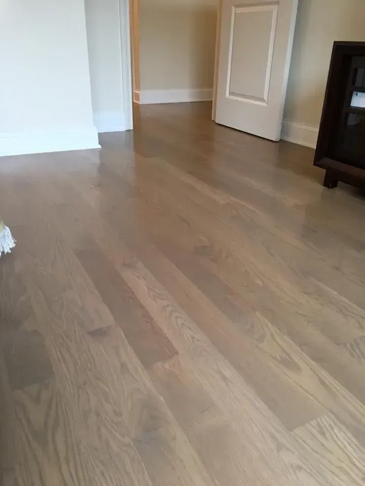 Light gray hardwood flooring in a room with white baseboards and a partially open white door in the background.