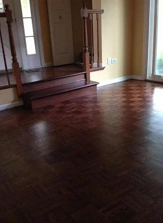 A dark parquet hardwood floor in a room leading up to a landing with wooden railings and white doors.