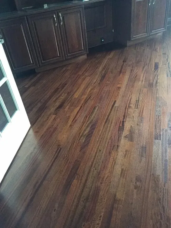 Polished dark-brown hardwood flooring in a room with dark wood cabinets and a white door frame.