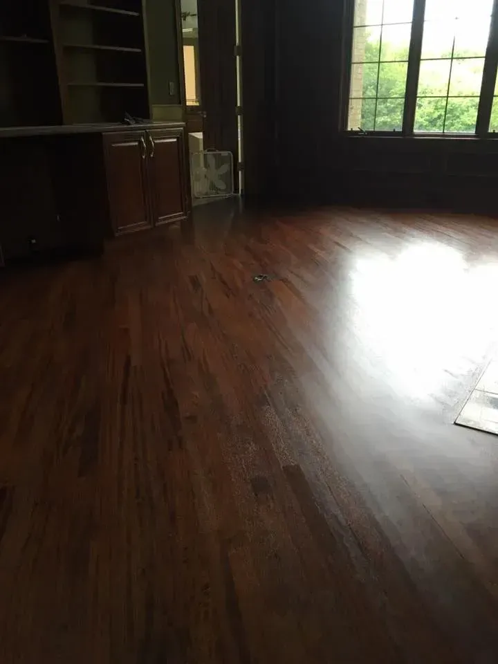 A polished dark hardwood floor in a room featuring built-in cabinetry and large windows with natural light.