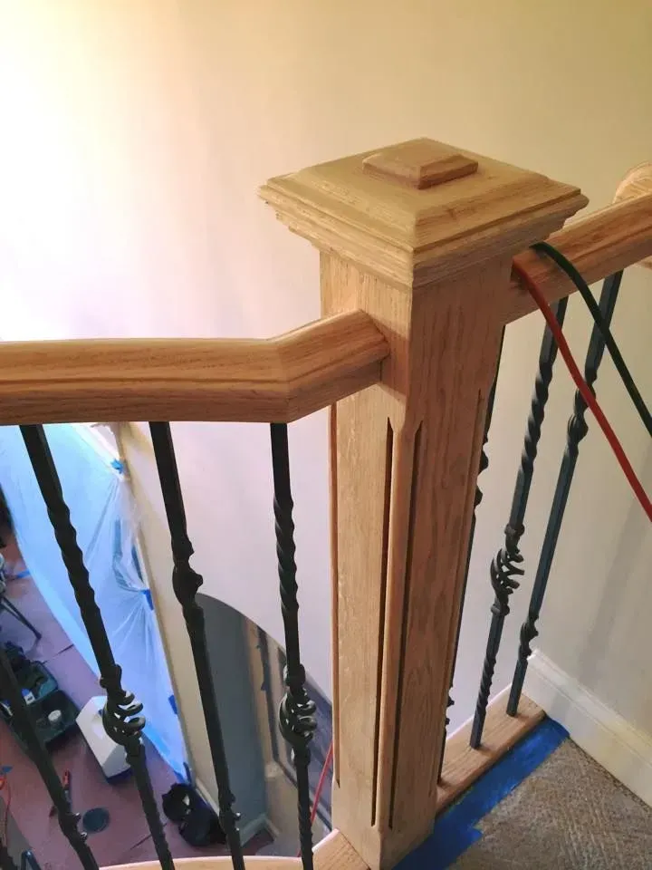 A wooden newel post on a staircase with decorative metal balusters and a handrail.