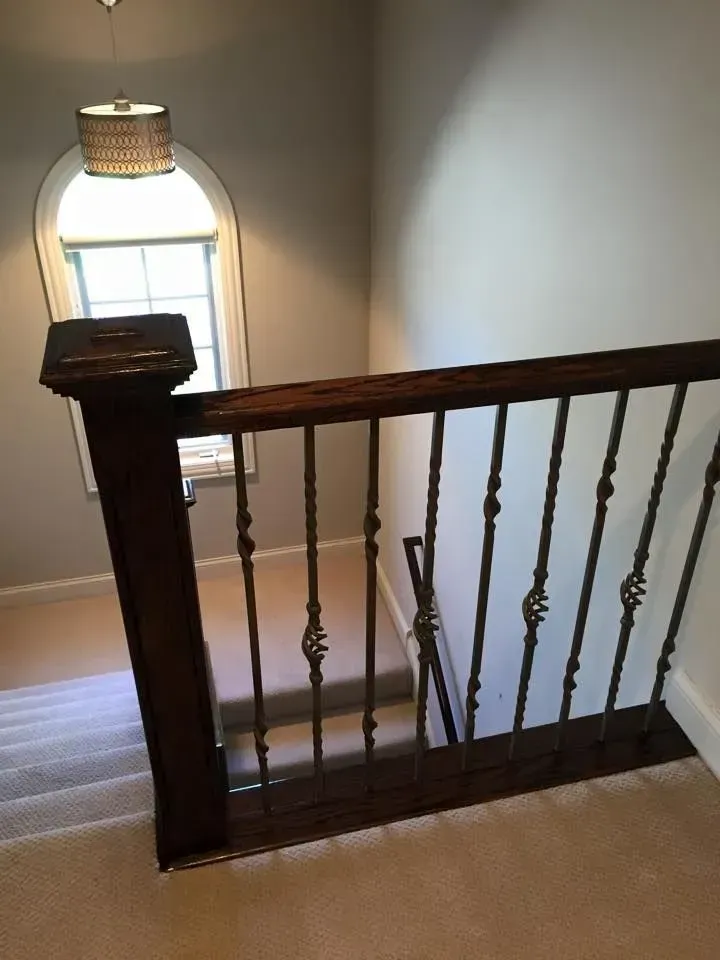 A wooden stair railing with decorative metal balusters overlooking a staircase near an arched window with a pendant light.
