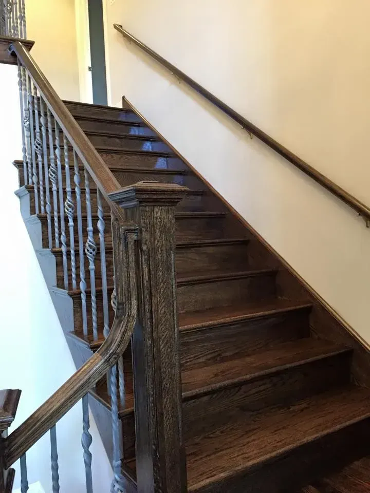 A staircase with dark wood treads and a handrail featuring decorative metal balusters against a plain white wall.