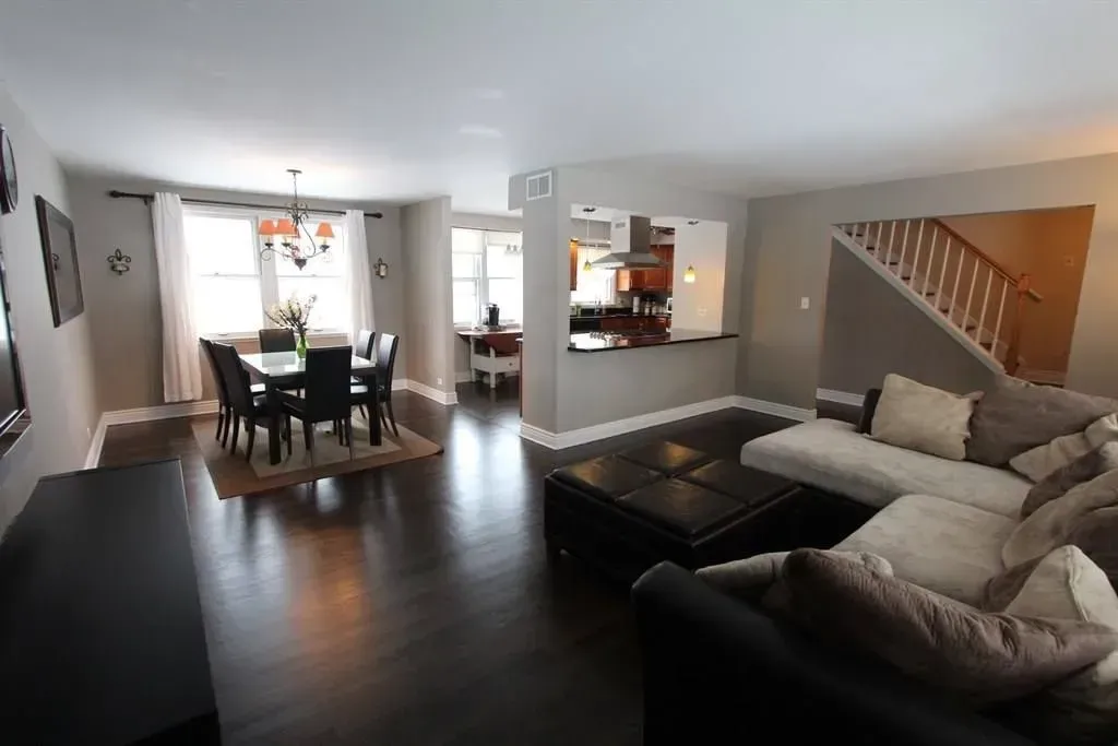 An open-concept interior featuring a dining area with a table and chairs, a kitchen cutout, and a living area with a sofa.