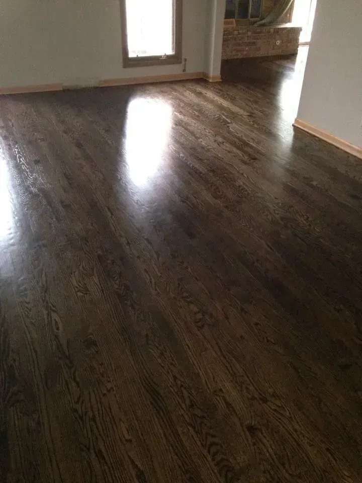 Dark stained hardwood floors in a well-lit residential room, reflecting light from a nearby window.