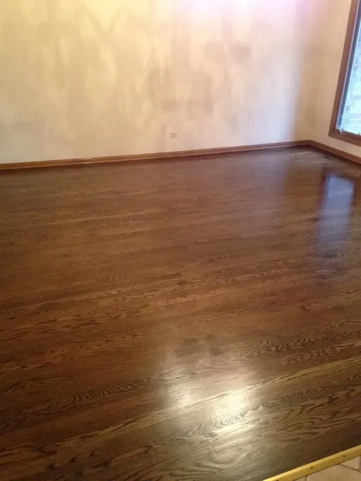 A room featuring freshly stained, dark brown hardwood floors and light-colored walls with wood trim.
