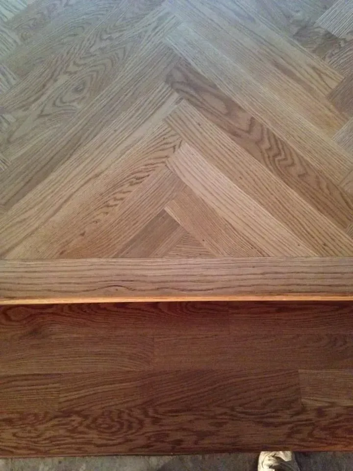 Light-colored oak herringbone flooring meeting a dark stained wooden threshold.