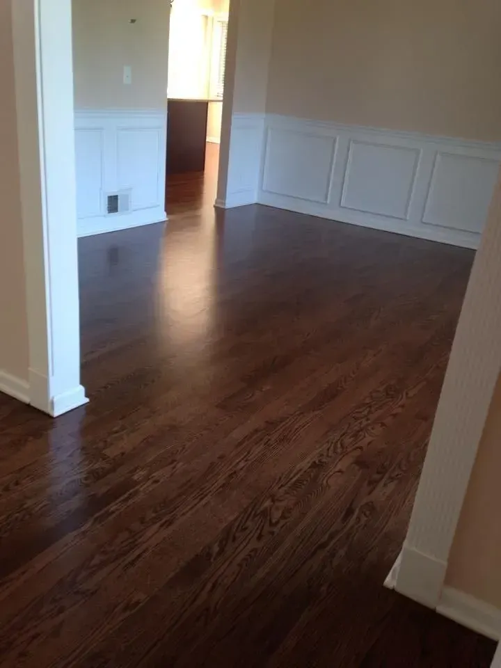 An interior view of a room with dark wood flooring, white wainscoting on the walls, and a doorway leading to another room.