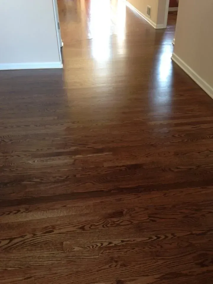 A brightly lit hallway with polished, dark brown hardwood floors leading into a distant room.