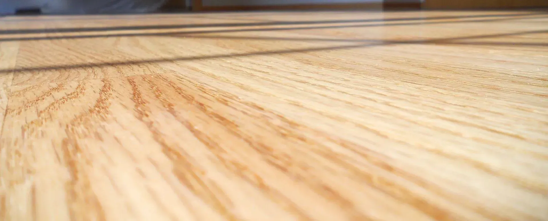 A close-up, angled view of light-colored wood flooring showing grain patterns and parallel shadows across the planks.