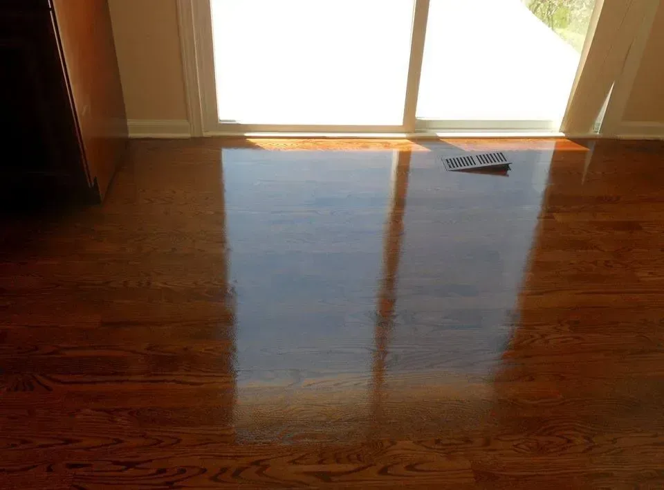 Polished dark hardwood floor reflecting a sliding glass door with a small black vent cover resting on the surface.