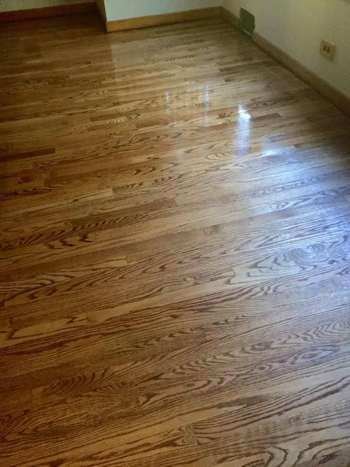 Polished light brown hardwood flooring with visible wood grain patterns in a room with white walls and baseboards.