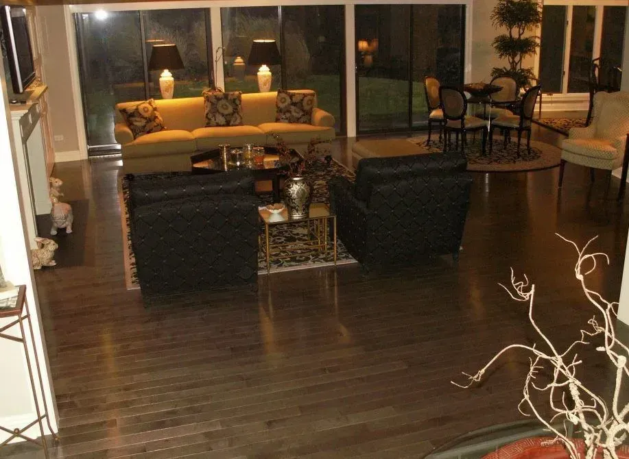 A spacious living room featuring a gold couch, two dark leather chairs, a small table, and a dining area in the back.