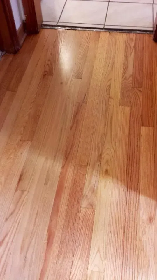 A perspective view of light-colored hardwood floor planks leading to a doorway with tiled flooring beyond.