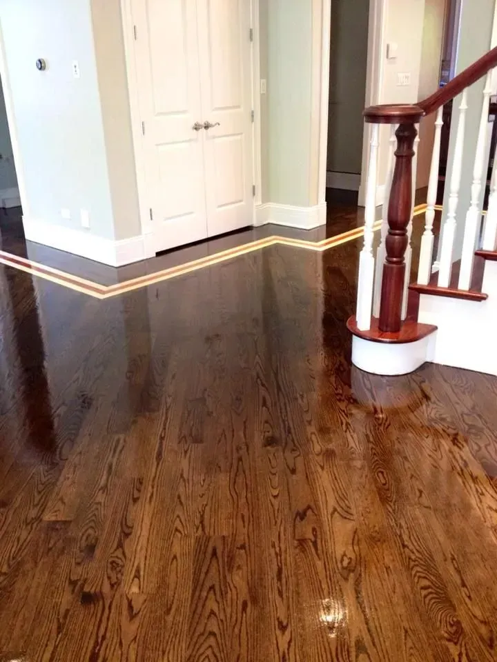 Polished dark hardwood floor with a decorative lighter wood border, leading to a white door and a staircase.
