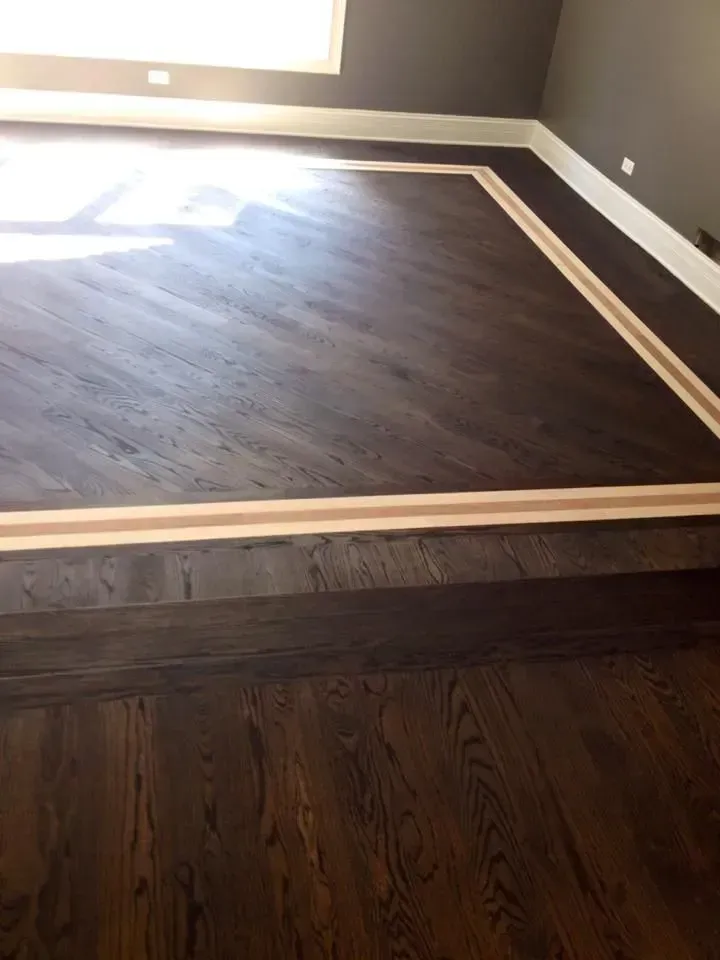 Dark wood flooring with a herringbone inlay pattern, separated by a light wood transition strip on a raised platform.