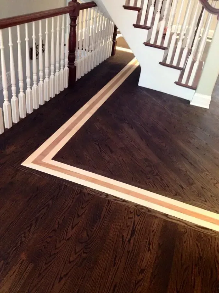 Dark wood floor with a decorative light wood border running along a staircase and railing.