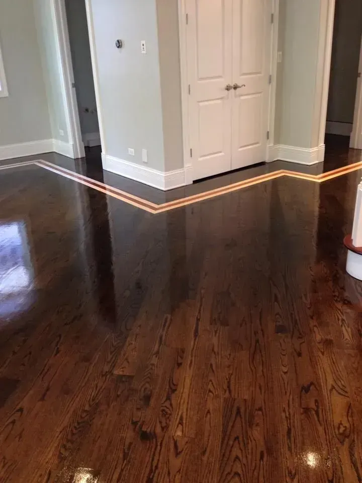 A polished dark wood floor features a decorative double inlay border that wraps around a corner wall.