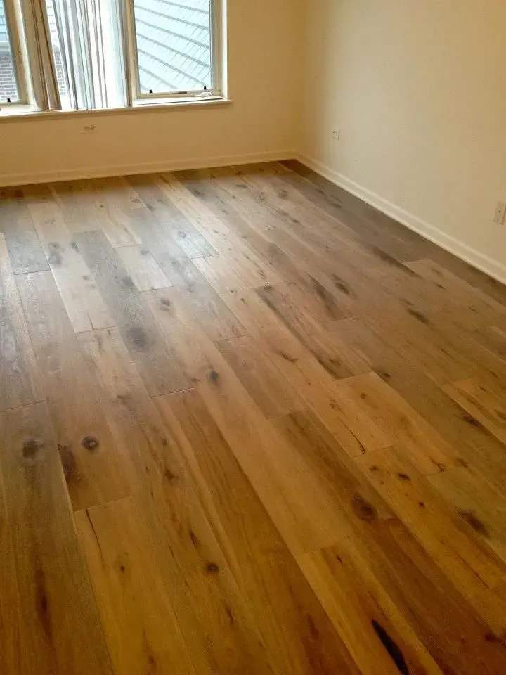A room with light-colored walls and a window, featuring wide-plank wood flooring with varied brown tones and visible grain.