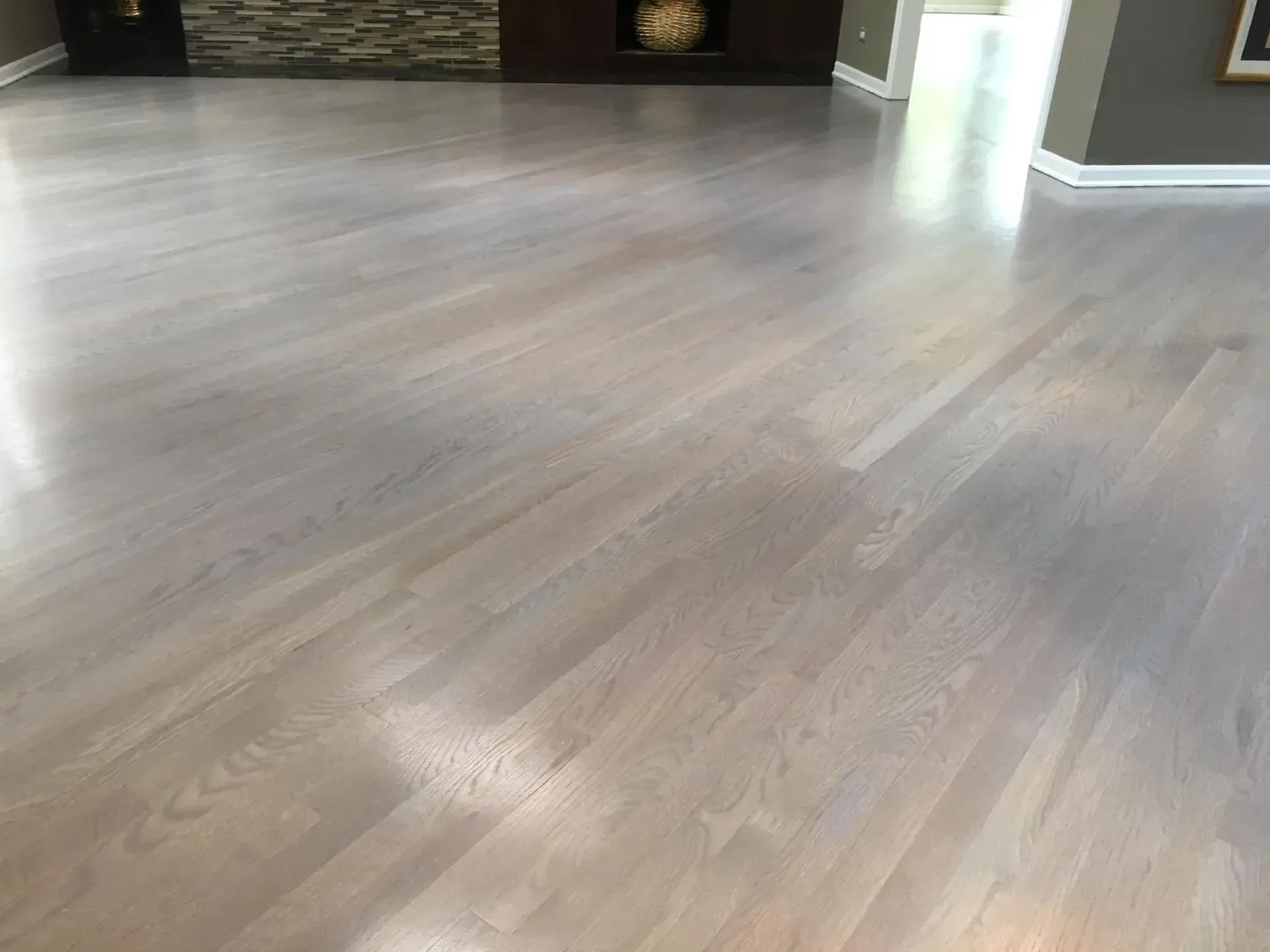 A bright, modern room featuring light-colored, grey-toned hardwood flooring with a visible wood grain pattern.